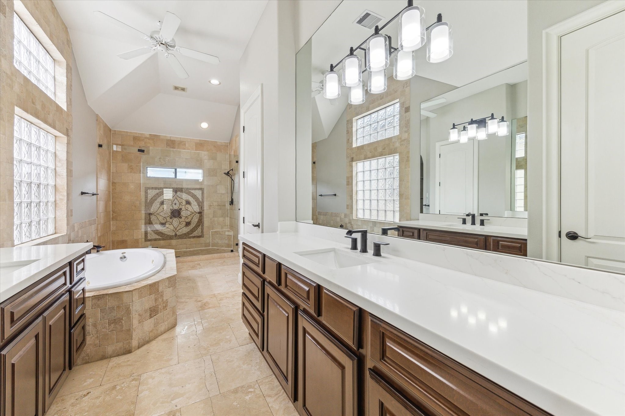 1512 Thompson Street, Unit 3 Houston, TX 77007 - Photo 18 of 32 This spacious bathroom features a luxurious design with a large soaking tub, dual sinks with elegant fixtures, ample cabinetry, and a separate shower. Natural light filters through glass block windows, enhancing the bright and airy atmosphere.