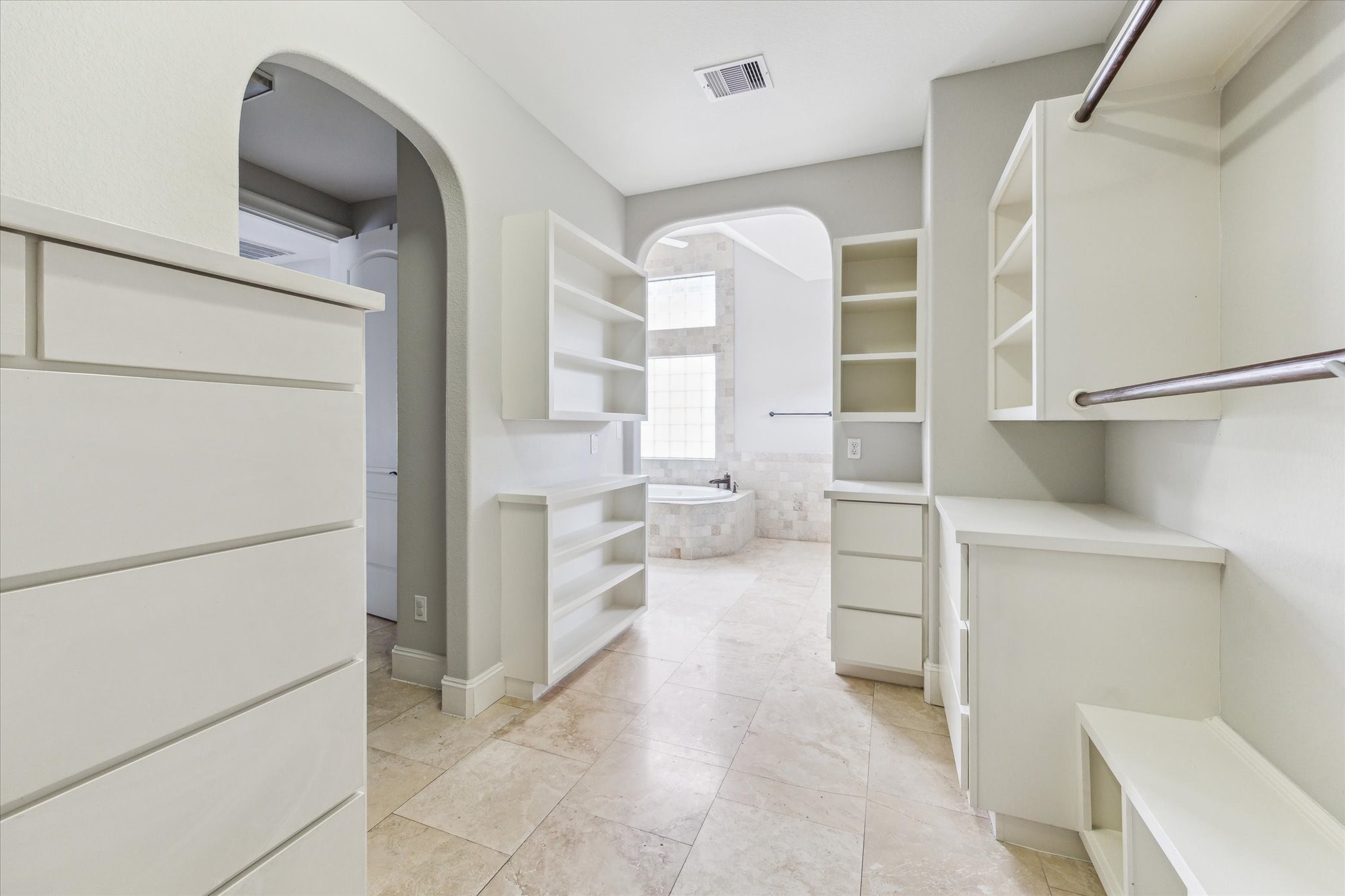 1512 Thompson Street, Unit 3 Houston, TX 77007 - Photo 21 of 32 A spacious, well-lit walk-in closet with ample shelving and storage. It features an arched doorway leading to a luxurious bathroom with a large window and a soaking tub.