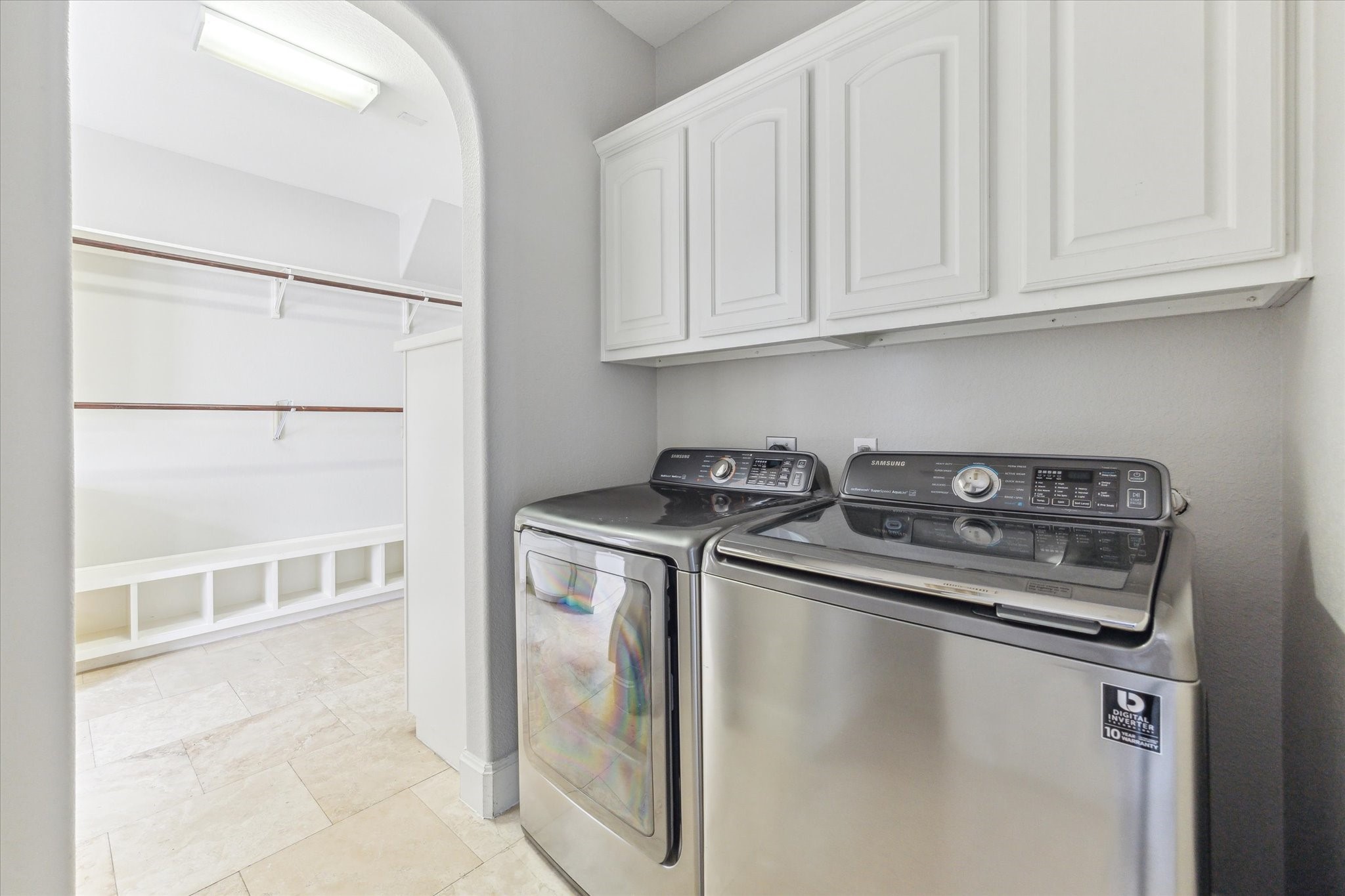 1512 Thompson Street, Unit 3 Houston, TX 77007 - Photo 23 of 32 Bright laundry room featuring stainless steel washer and dryer units, with white cabinets above for storage and an open walk-in closet area adjacent for organization.