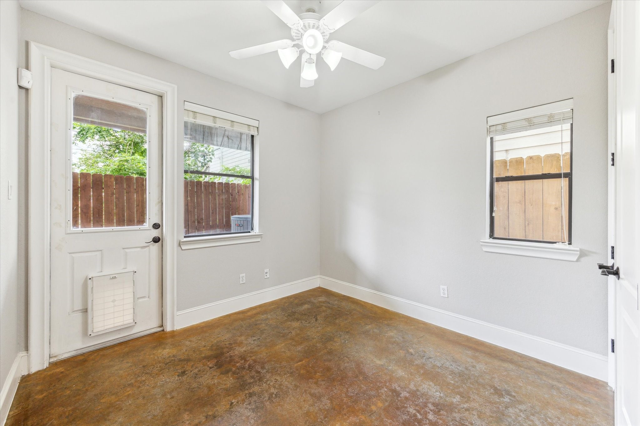 1512 Thompson Street, Unit 3 Houston, TX 77007 - Photo 25 of 32 Bright room with concrete floors, neutral walls, and a ceiling fan. It features a door with a pet flap for outdoor access to the turfed backyard.