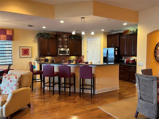 a kitchen with stainless steel appliances kitchen island granite countertop a refrigerator a stove a sink and a dining table with wooden floor