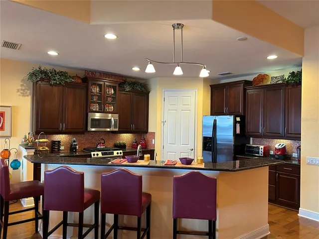 a kitchen with stainless steel appliances granite countertop a refrigerator a stove a sink a dining table and chairs with wooden floor