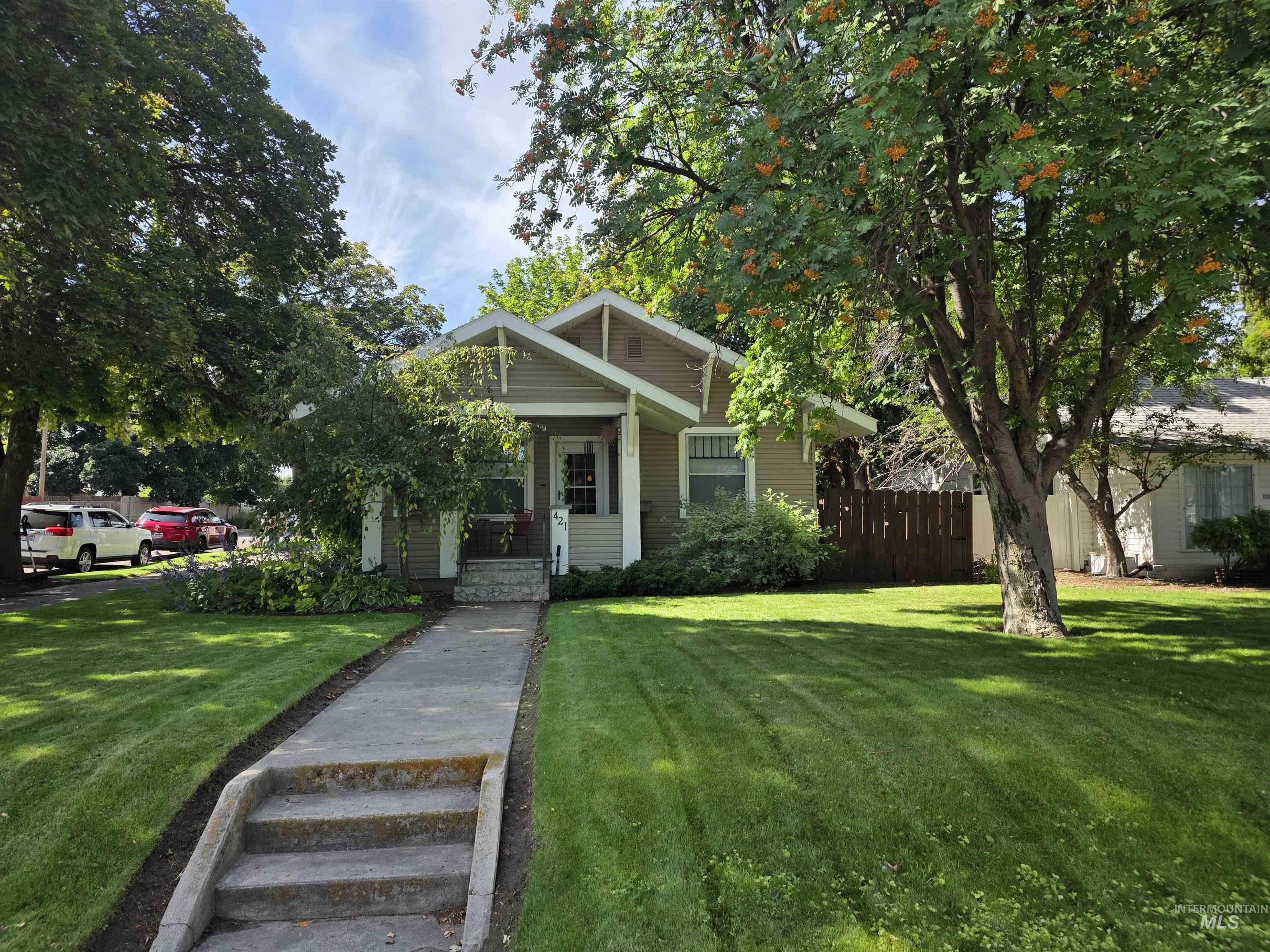 421 East Main Street Jerome, ID 83338 - Photo 1 of 13 Craftsman-style home featuring a gabled roofline, front porch, mature trees, concrete walkway, and a neatly manicured lawn
