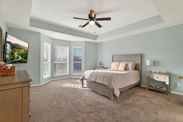a spacious bedroom with a bed and a flat tv screen on dresser
