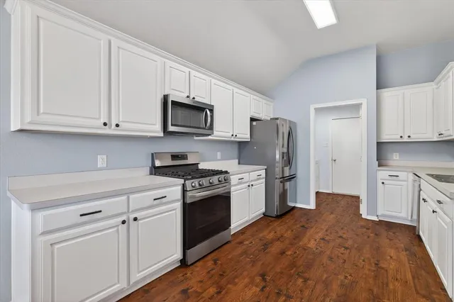 a kitchen with stainless steel appliances granite countertop white cabinets a sink a stove a refrigerator and microwave with wooden floor