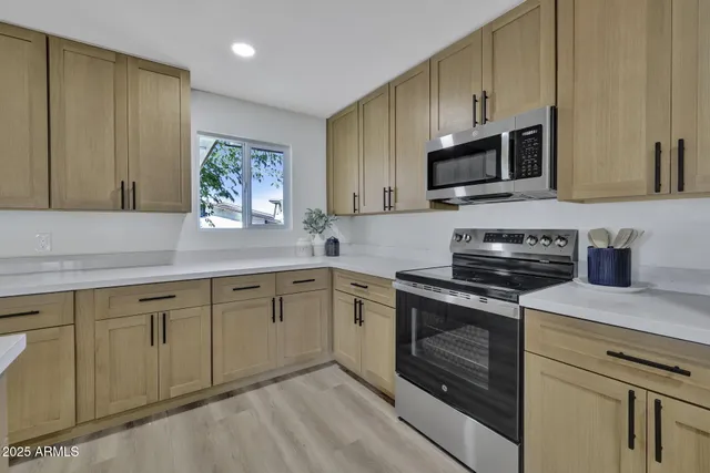 a kitchen with stainless steel appliances granite countertop white cabinets a sink a stove a microwave and wooden floors