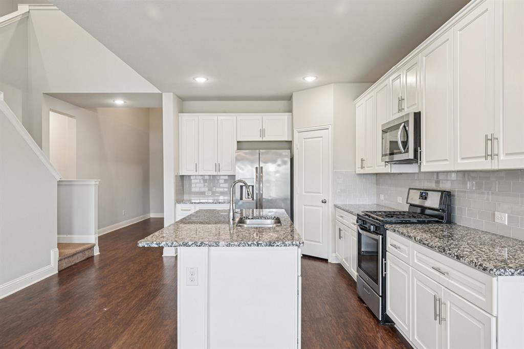 2321 Mount Olive Lane Forney, TX 75126 - Photo 14 of 35 Kitchen featuring stainless steel appliances, dark wood-type flooring, light stone countertops, white cabinets, and a kitchen island with sink