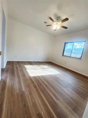 an empty room with wooden floor chandelier fan and windows