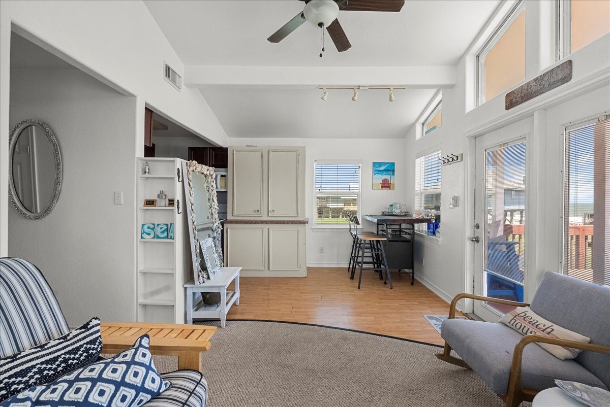 819 Seashell Drive Surfside Beach, TX 77541 - Photo 26 of 36 This bright and airy living space features high ceilings, ample natural light from large windows, and a cozy seating area. The room opens to a small dining nook and includes charming beach-themed decor. A ceiling fan and light wood flooring enhance the inviting atmosphere, making it a perfect spot for relaxation and entertaining.