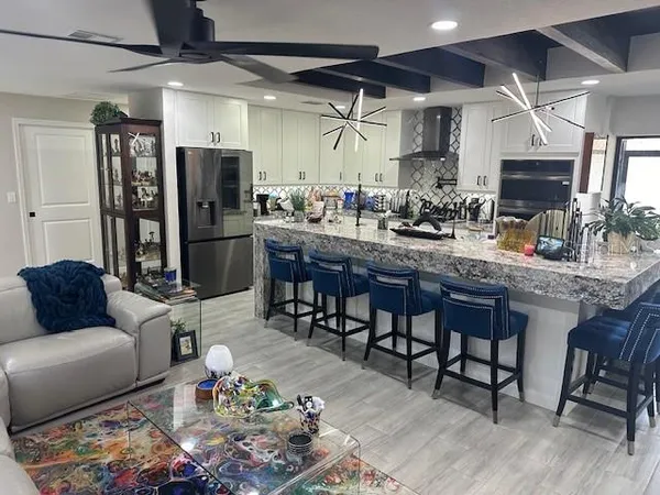 a kitchen with stainless steel appliances kitchen island granite countertop a refrigerator a sink a dining table and chairs with wooden floor
