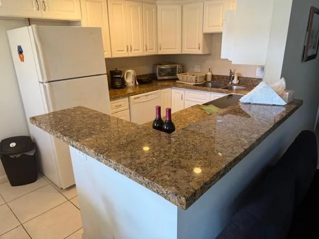 a kitchen with granite countertop a refrigerator a stove a sink and white cabinets