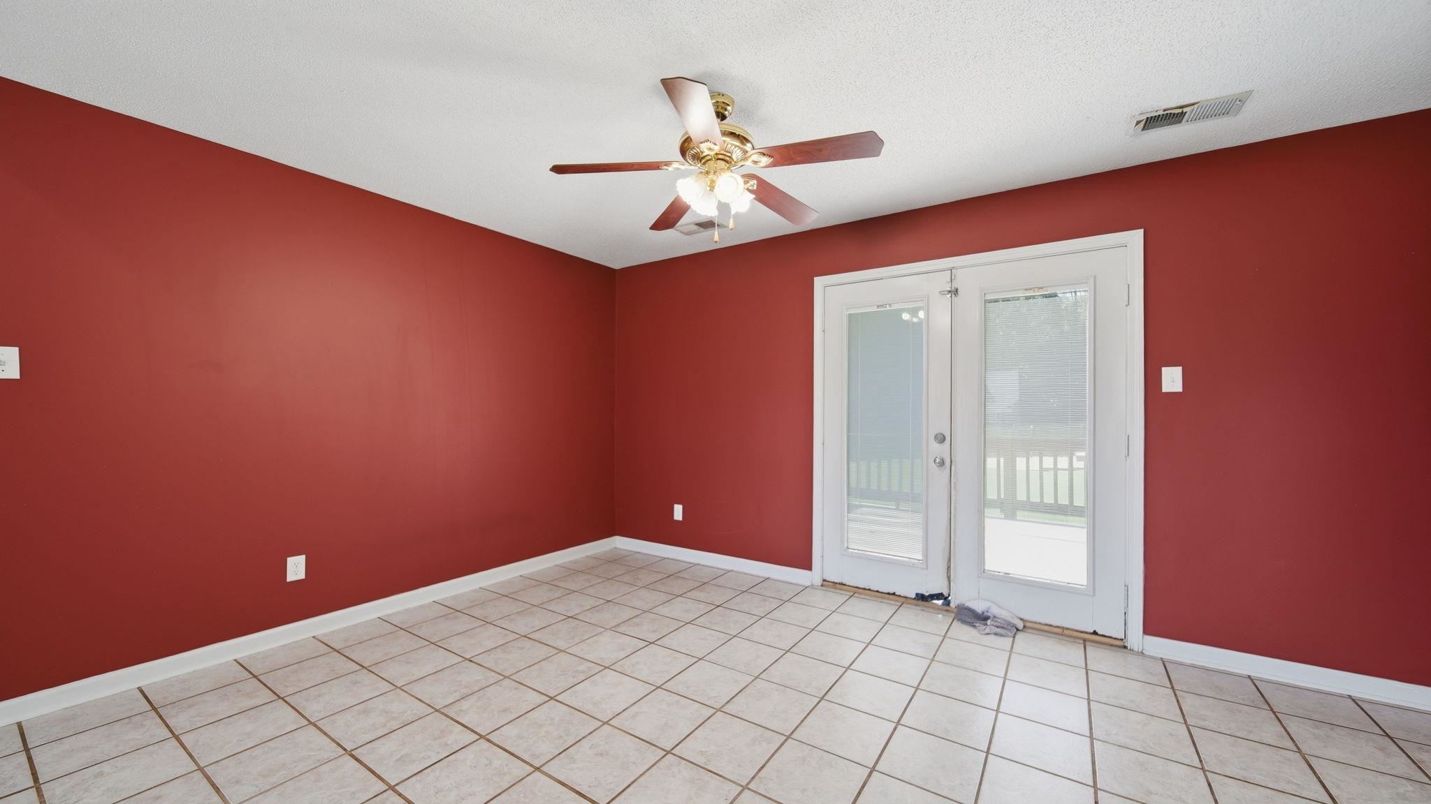 217 Rae Drive Munford, TN 38058 - Photo 10 of 40 Spacious room featuring neutral tile flooring, vibrant accent walls, a ceiling fan with light fixture, and white French doors opening to an exterior deck