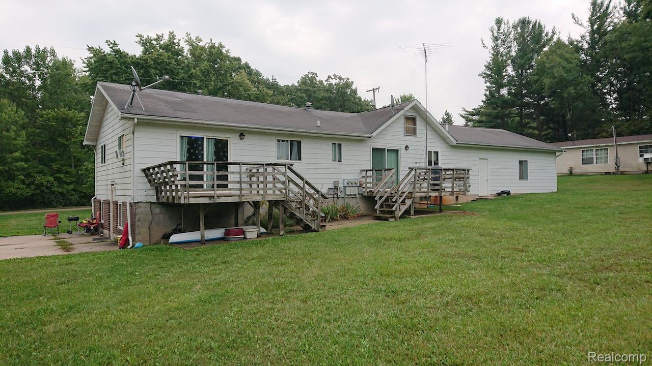 White siding exterior with multiple wooden decks, a concrete patio, and a sloped grass yard