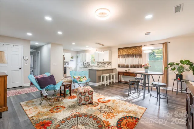 a living room with furniture a rug kitchen view and a large window