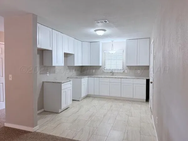 a large white kitchen with granite countertop white cabinets and stainless steel appliances