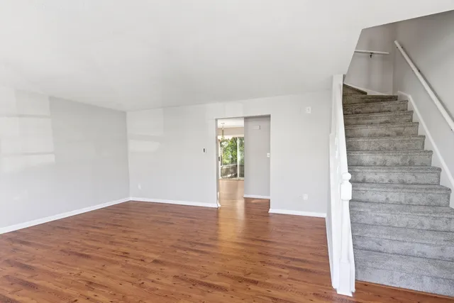 a view of an empty room with wooden floor and stairs