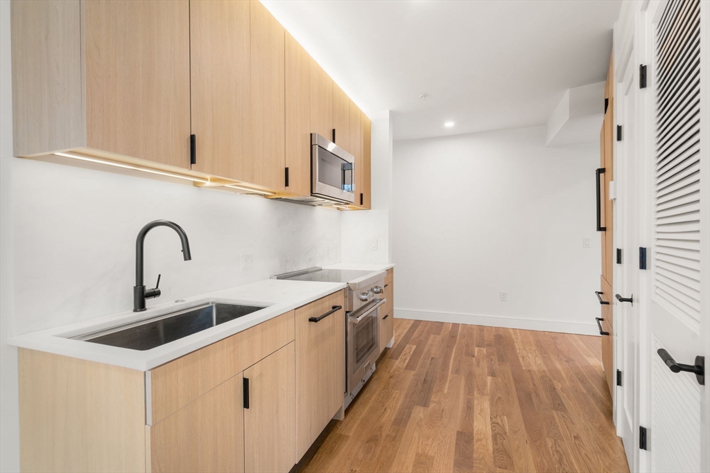 58 Kent, Unit 304 Brookline, MA 02445 - Photo 2 of 19 a view of a kitchen with kitchen island a sink wooden floor and stainless steel appliances