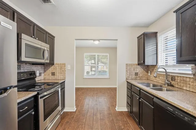 a kitchen with granite countertop a sink wooden floor and stainless steel appliances