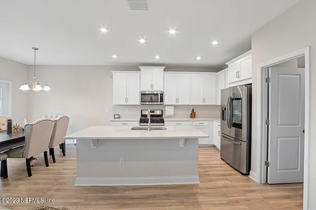 a large kitchen with stainless steel appliances kitchen island a stove a refrigerator a sink dishwasher a dining table and chairs with wooden floor