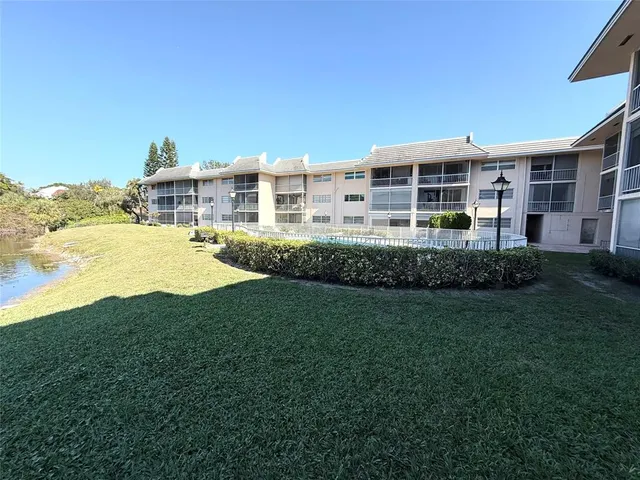 a view of a house next to a big yard with plants and large trees