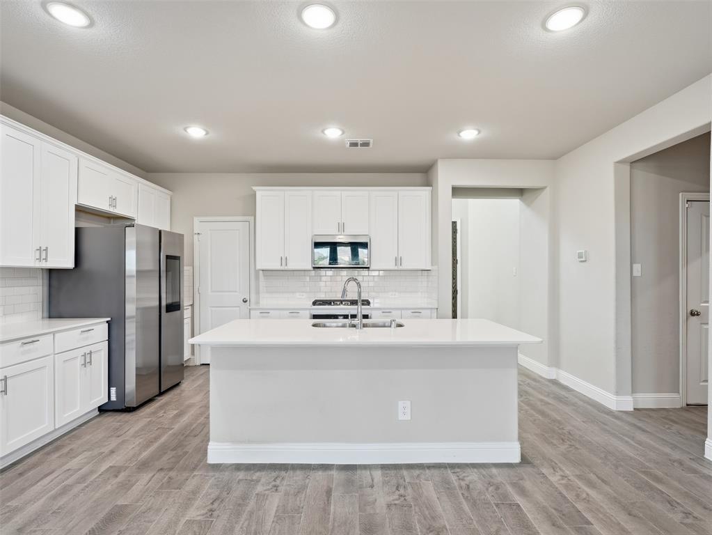 1128 Red Hawk Lane Forney, TX 75126 - Photo 8 of 37 Kitchen featuring wood-finish flooring, white cabinetry, a central island, and stainless steel appliances