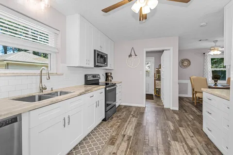 a kitchen with a sink dishwasher a stove and white cabinets with wooden floor