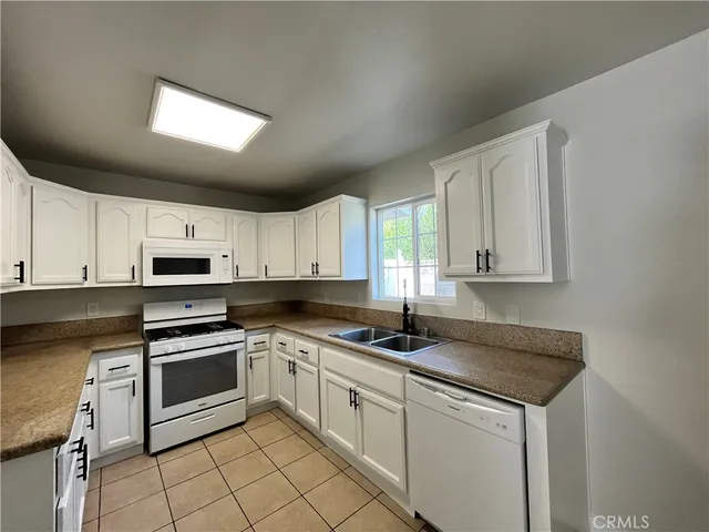 a kitchen with granite countertop a sink stainless steel appliances white cabinets and a window
