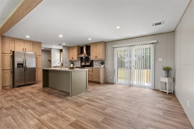 a kitchen with stainless steel appliances kitchen island granite countertop a refrigerator oven a sink with wooden cabinets and wooden floor