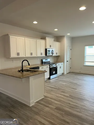 a large kitchen with stainless steel appliances granite countertop a stove a sink a refrigerator and white cabinets with wooden floor