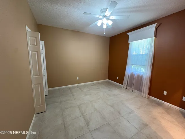 an empty room with chandelier fan and windows