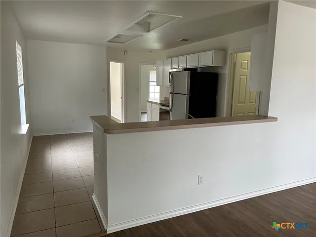 a view of a refrigerator in kitchen and an empty room