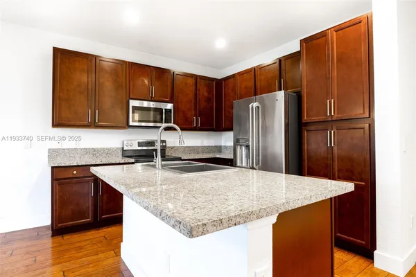 a kitchen with stainless steel appliances granite countertop a refrigerator a stove and a sink with wooden floor