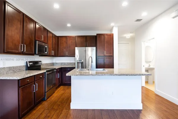 a kitchen with stainless steel appliances granite countertop a stove a refrigerator a sink a oven with wooden cabinets and wooden floor
