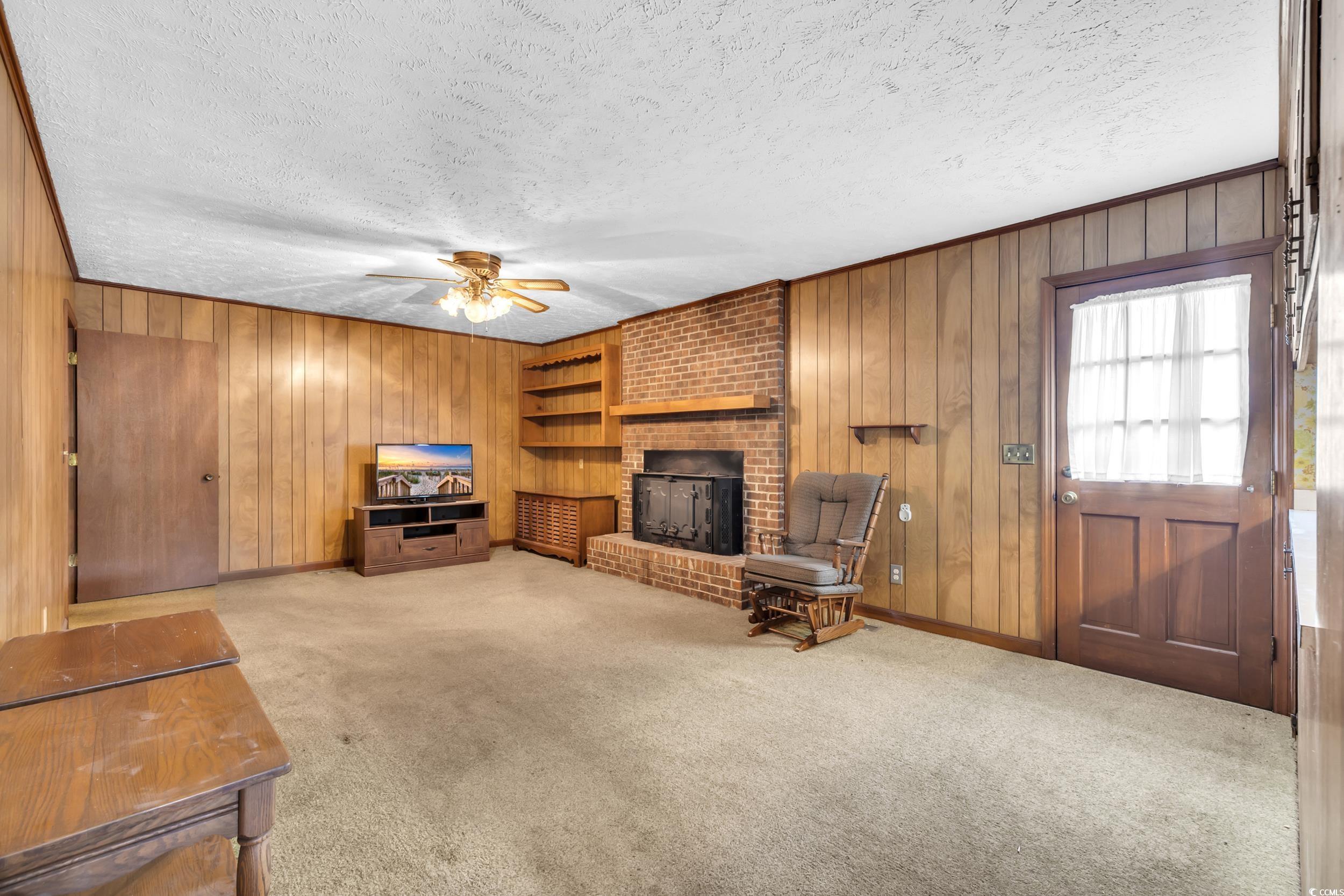 1928 Emery Road Loris, SC 29569 - Photo 3 of 24 Living room with light carpet, wood walls, a fireplace, a textured ceiling, and ceiling fan