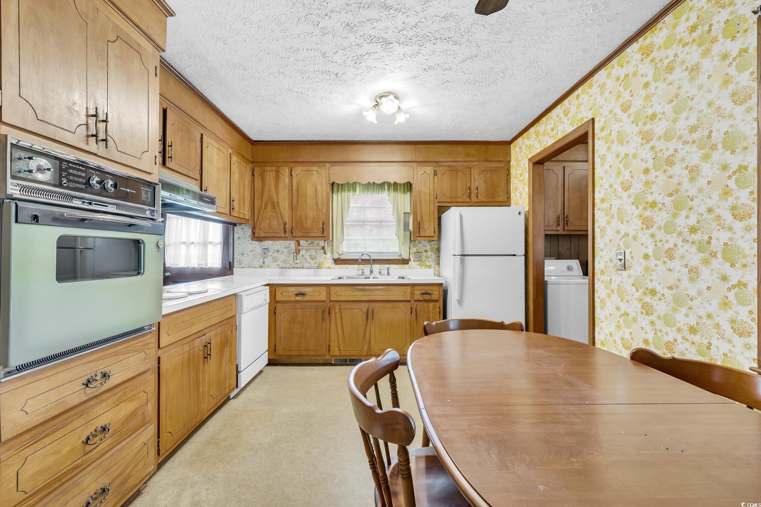 1928 Emery Road Loris, SC 29569 - Photo 6 of 24 Kitchen featuring wallpapered walls, light countertops, white appliances, brown cabinets, and washer / clothes dryer