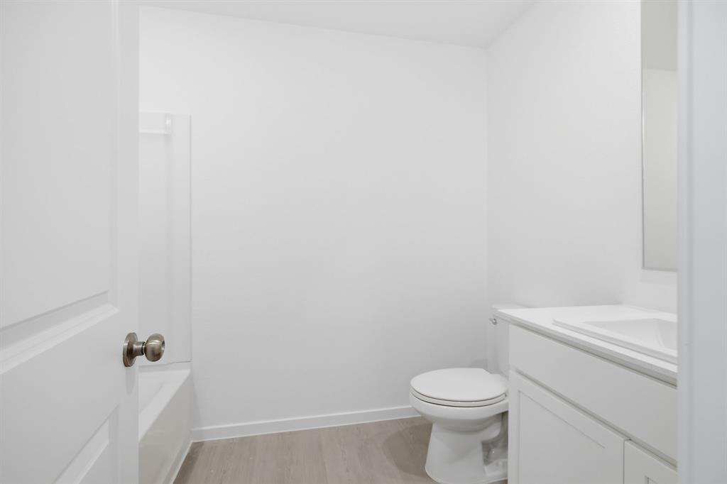 2128 Doc Holliday Road Joshua, TX 76058 - Photo 6 of 28 Bathroom featuring white walls, wood-finish flooring, a white vanity with an integrated sink, a matching white toilet, and a white bathtub with a shower surround