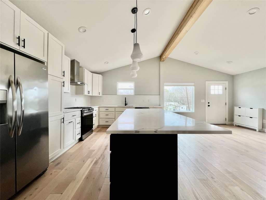a kitchen with stainless steel appliances kitchen island granite countertop a refrigerator a sink dishwasher a stove and white cabinets with wooden floor