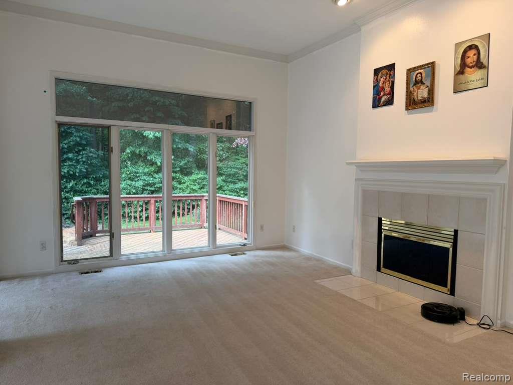1154 Bluebird Drive Rochester, MI 48307 - Photo 6 of 34 Spacious room featuring a fireplace with a tiled surround and mantel, light-toned carpeting, and a large multi-panel glass door with an upper transom window opening to an exterior deck