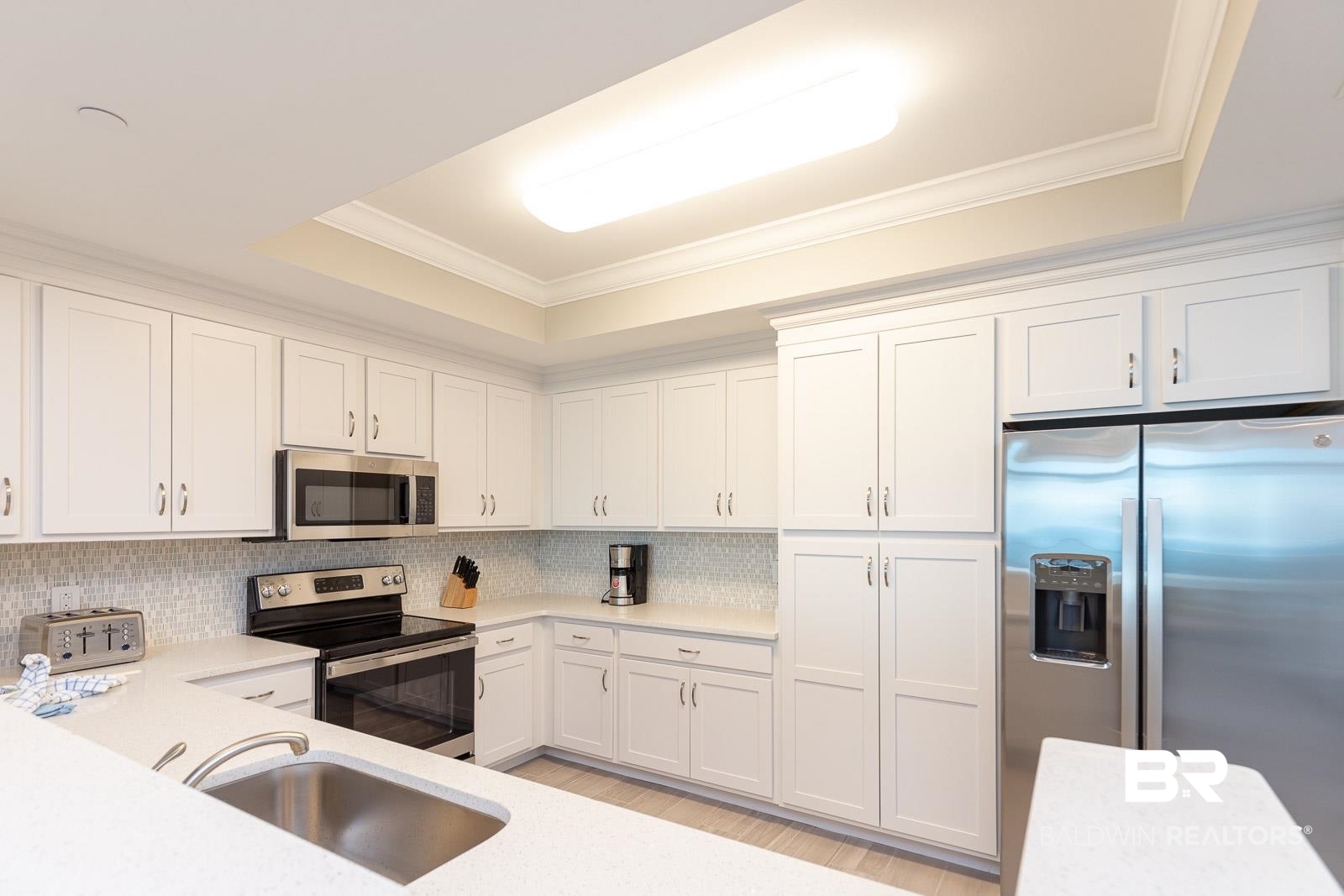 23008 Perdido Beach Boulevard, Unit 2003 Orange Beach, AL 36561 - Photo 7 of 35 Kitchen featuring tasteful backsplash, a tray ceiling, light hardwood / wood-style floors, appliances with stainless steel finishes, and sink