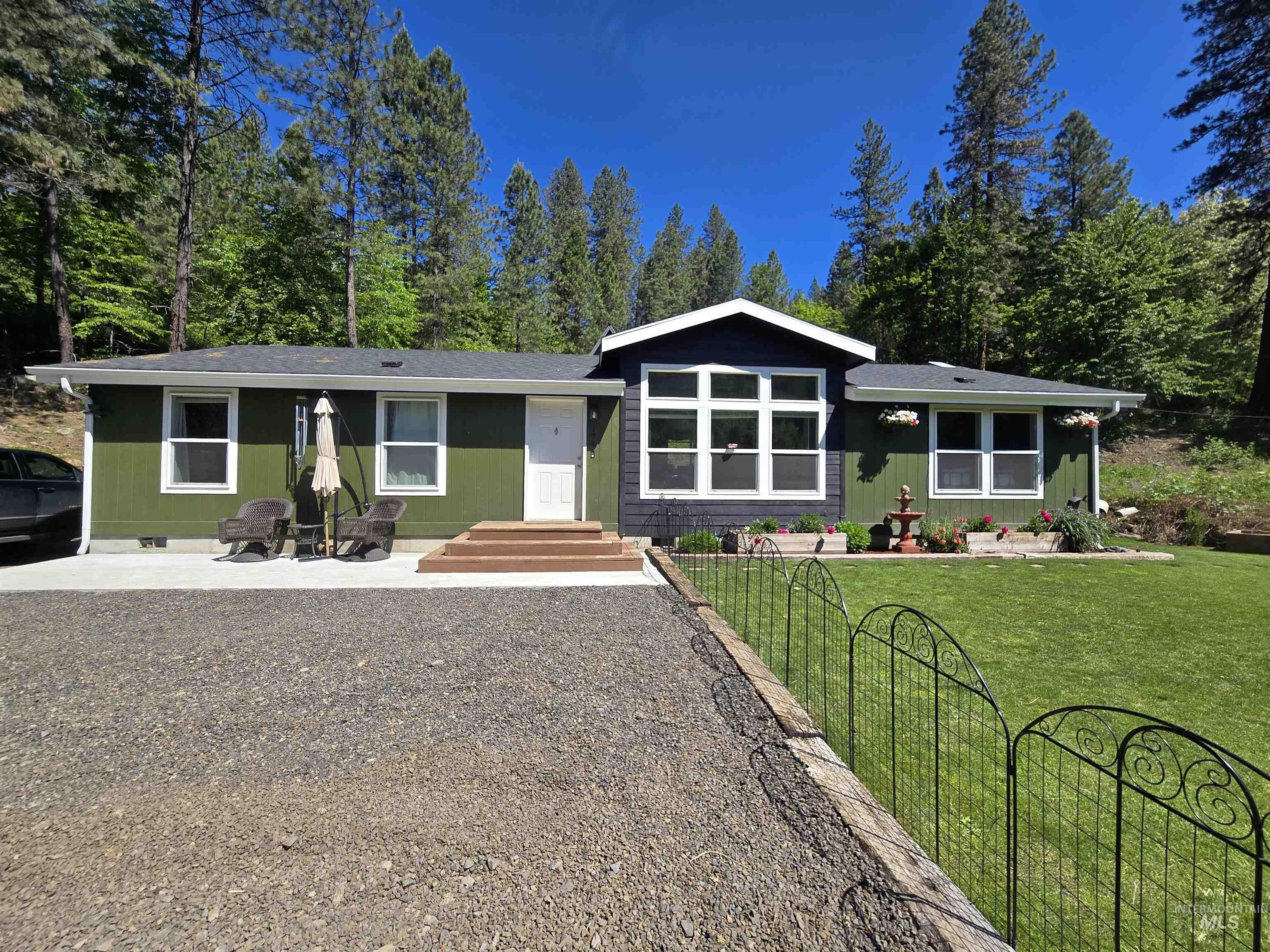 Single-story residence featuring green siding with white trim, a dark blue accent facade with large windows, a gravel driveway, and a front lawn with a decorative fence