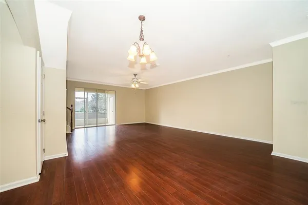 an empty room with wooden floor chandelier and windows