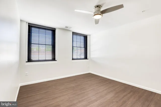 an empty room with wooden floor ceiling fan and windows