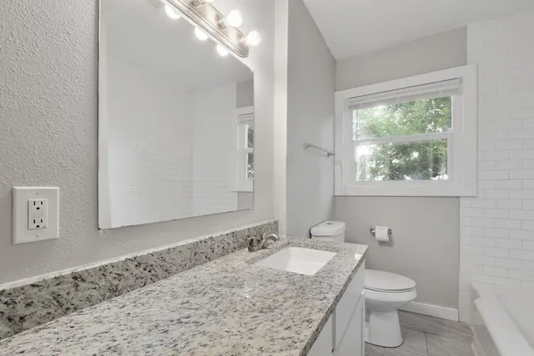 a bathroom with a granite countertop sink a toilet and a window