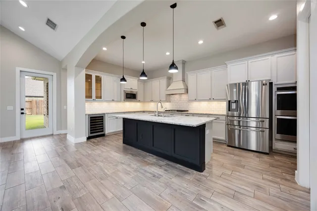 a kitchen with stainless steel appliances kitchen island granite countertop a refrigerator a oven a sink and white cabinets with wooden floor