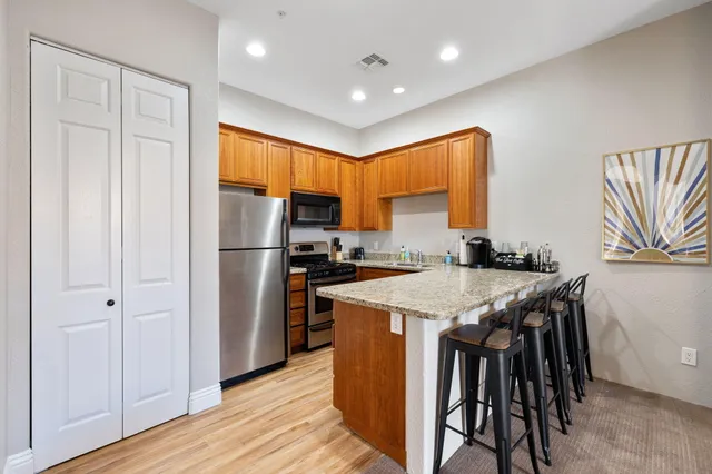 a kitchen with stainless steel appliances granite countertop a refrigerator a sink dishwasher a stove and a dining table with wooden floor