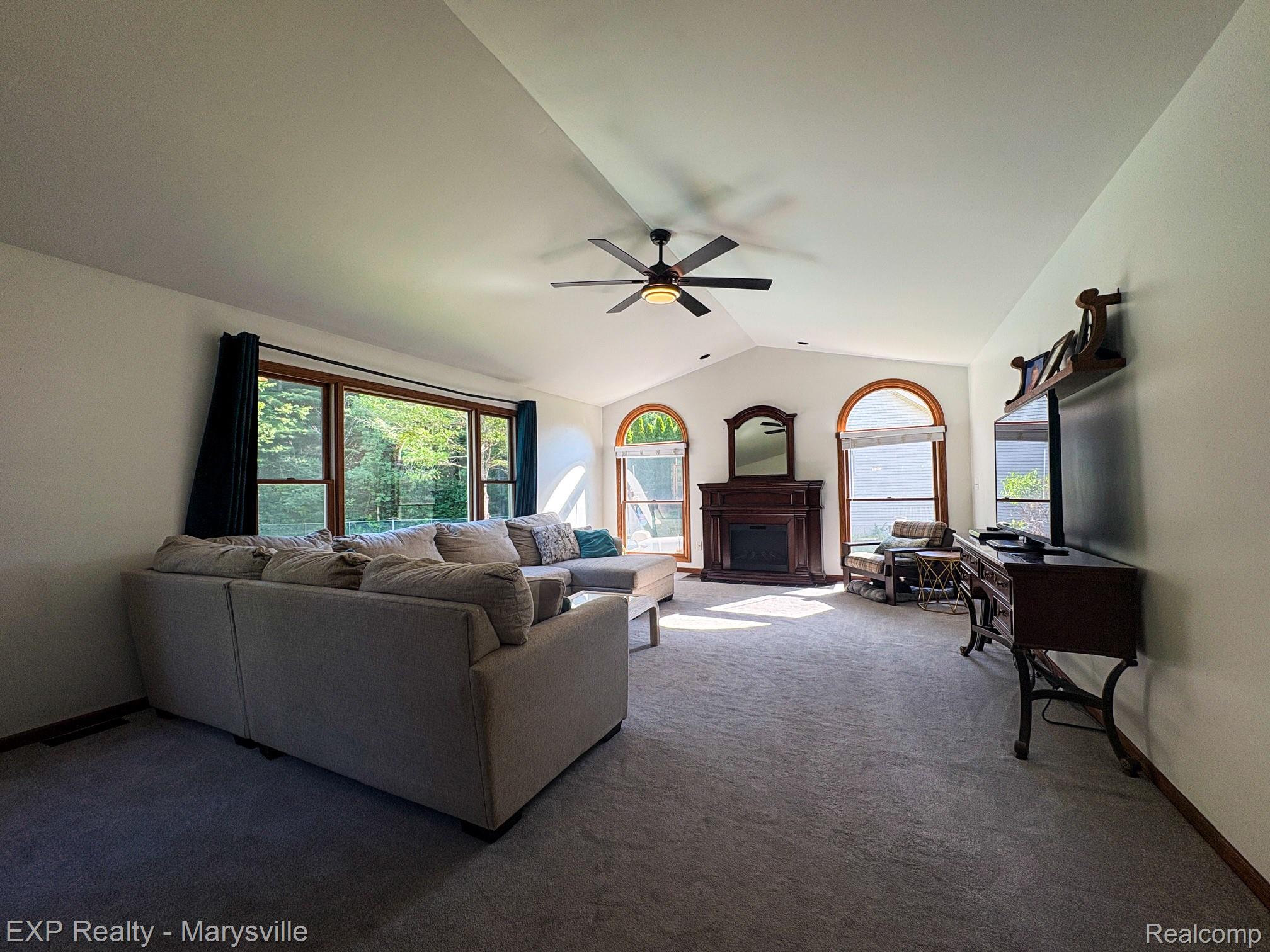 5538 Klettner Road St. Clair, MI 48079 - Photo 17 of 46 Spacious living area featuring vaulted ceilings with a ceiling fan, a prominent fireplace with a wood mantel, large rectangular windows, and two arched windows