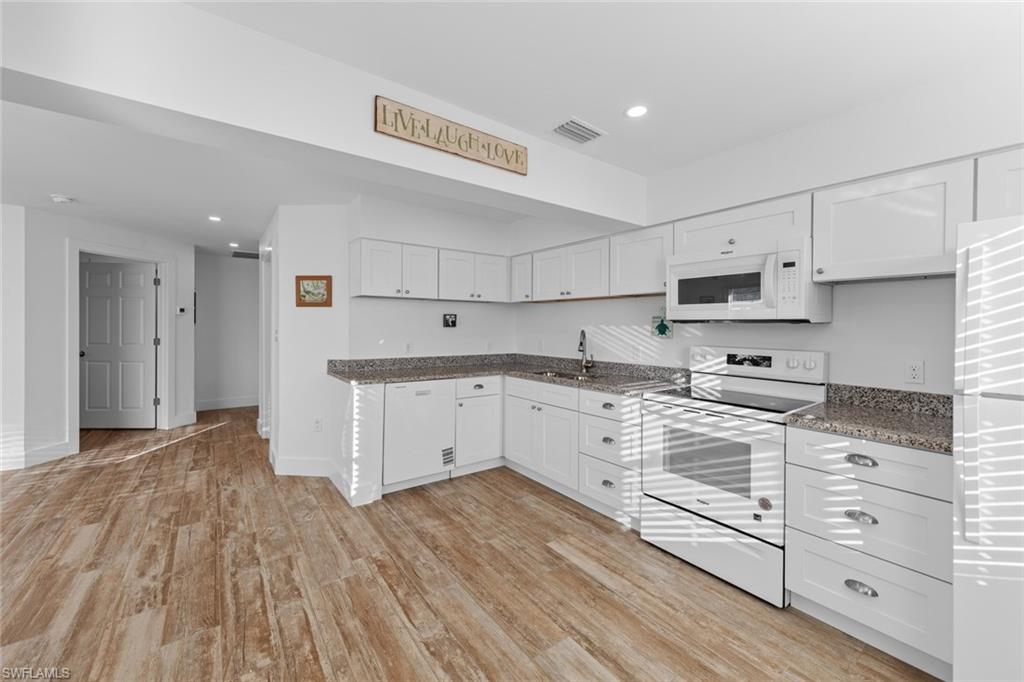 849 Beach Road Sanibel, FL 33957 - Photo 9 of 27 a kitchen with granite countertop a stove a sink and white cabinets with wooden floor