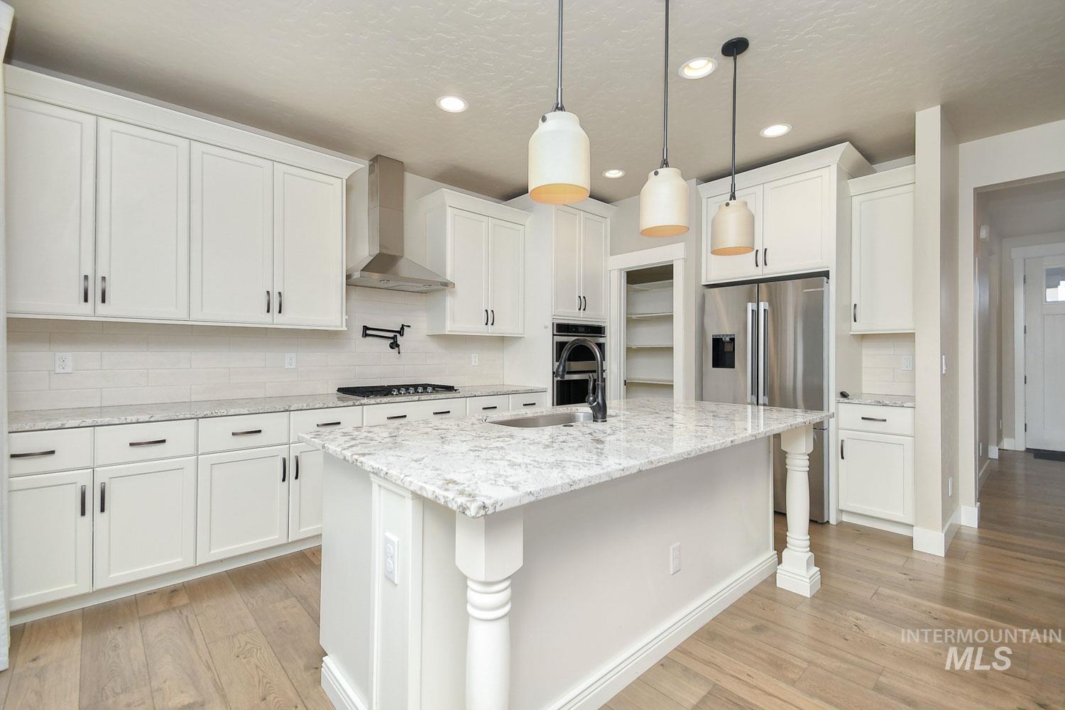 5771 West Daphne Drive Meridian, ID 83646 - Photo 12 of 32 Kitchen featuring decorative backsplash, wall chimney range hood, light stone counters, light wood-style flooring, and a kitchen island with sink