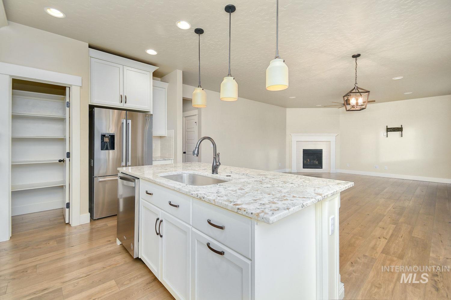 5771 West Daphne Drive Meridian, ID 83646 - Photo 13 of 32 Kitchen featuring white cabinets, hanging light fixtures, light wood finished floors, an island with sink, and recessed lighting