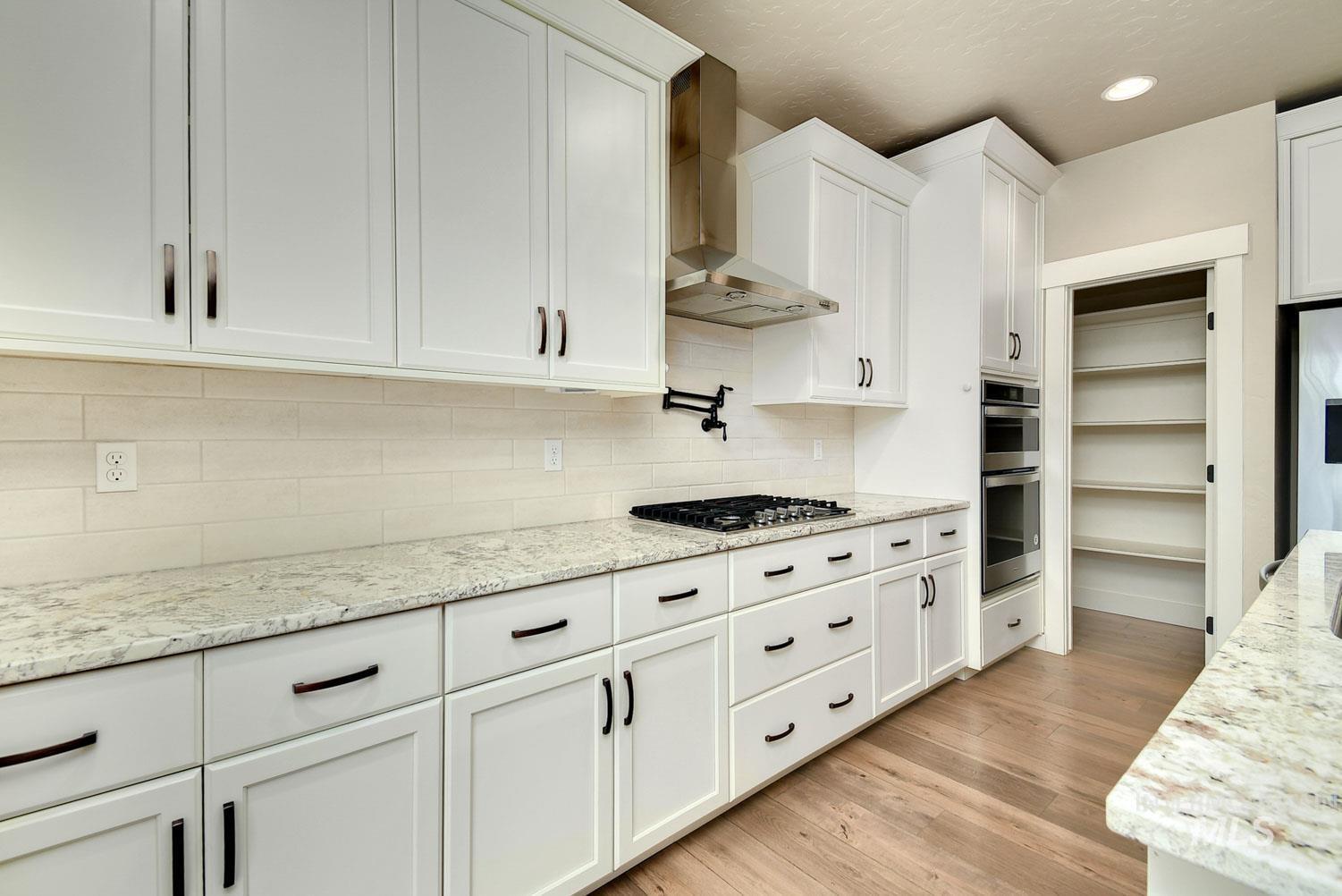 5771 West Daphne Drive Meridian, ID 83646 - Photo 14 of 32 Kitchen with wall chimney range hood, white cabinetry, light stone countertops, light wood-type flooring, and recessed lighting